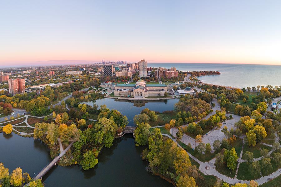 About Us - Aerial View of University Campus, Lakes, and Chicago Skyline at Dusk, the Trees Below Turning Colors in the Fall