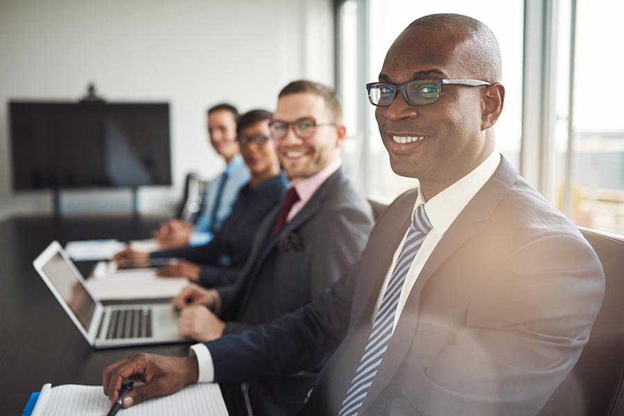 Employee Benefits - Employees at a Law Firm Smile at the Camera While Sitting at a Conference Table, Large Windows to Their Right